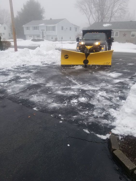 A yellow snow plow is plowing snow in a parking lot