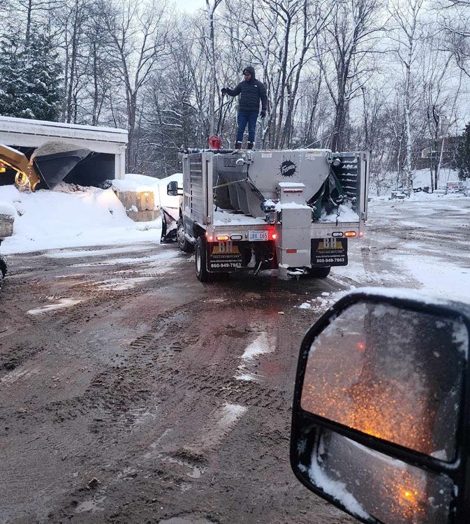 A truck with a man on top driving down a snowy road