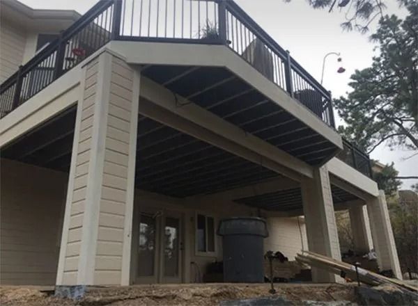 A two-story house with a deck. The deck is supported by pillars and has black railings. The underside of the deck is visible.