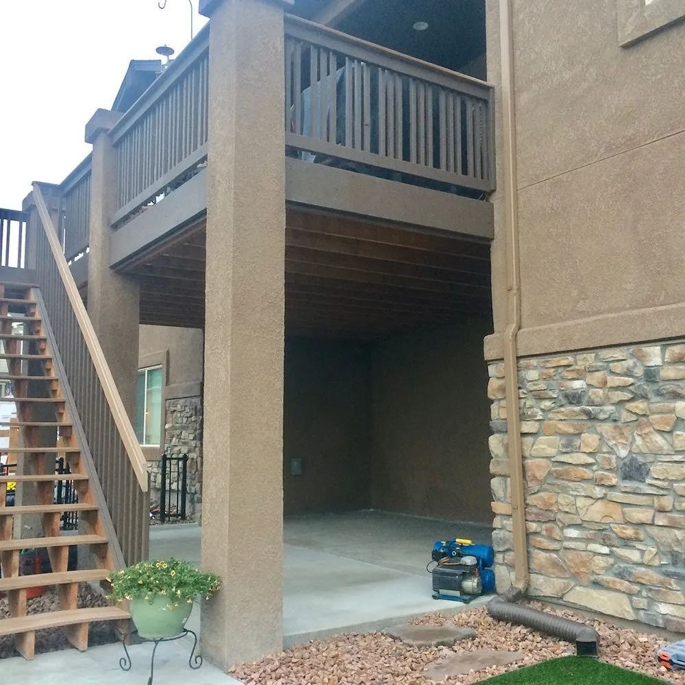 A two-story deck with a lower level open to a concrete surface. Stairs lead to the upper deck. The house exterior is tan.