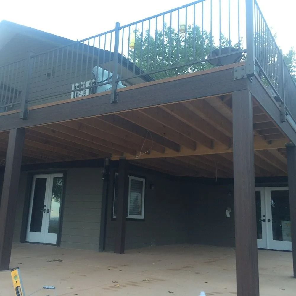 Multi-level home with a dark brown deck, railing, and supports. The ground level has doors and windows.