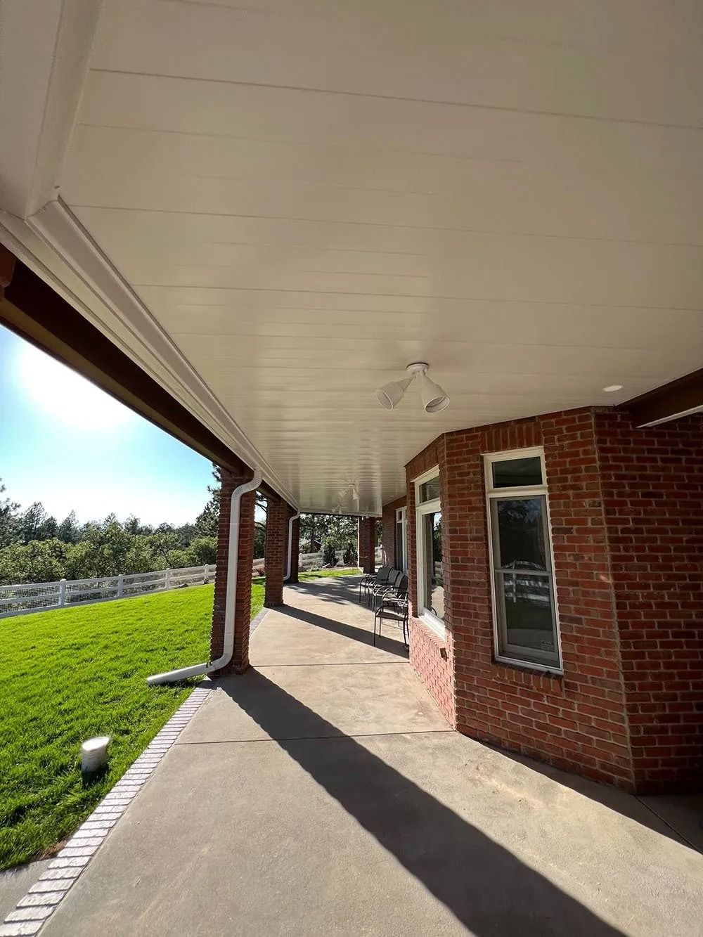 A brick building with a covered porch. The porch has a white ceiling, a concrete floor, and overlooks a grassy area.