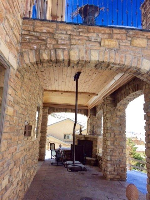 Stone patio with arched openings. A fireplace sits at the back. A swing hangs from the ceiling.