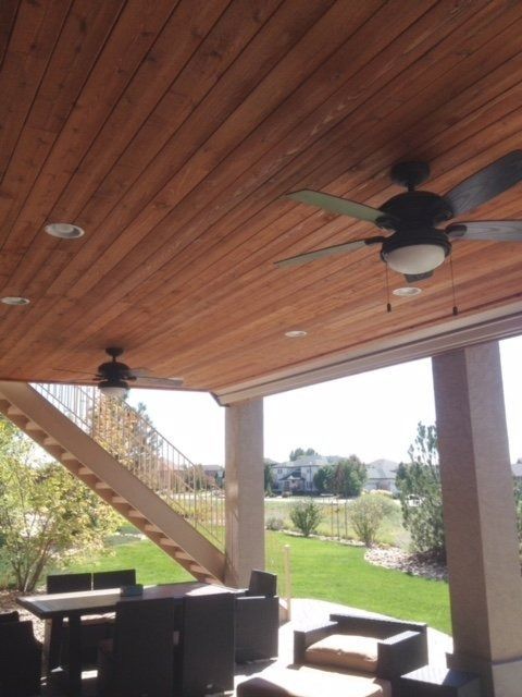 Wooden patio ceiling with two ceiling fans, overlooking a backyard with seating.