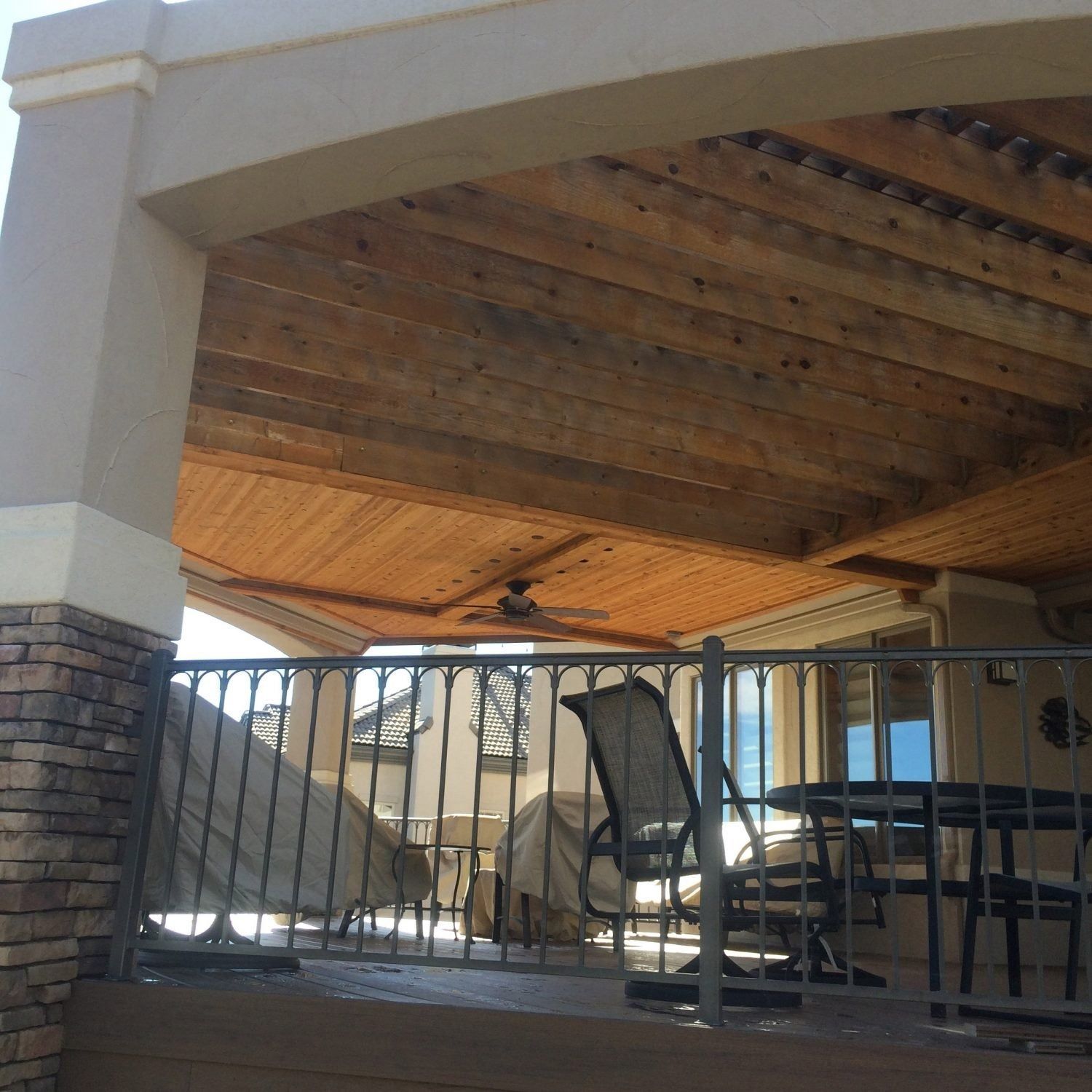 Patio with a wooden ceiling, a ceiling fan, and a wrought iron railing. Two covered chairs and a small table are visible.