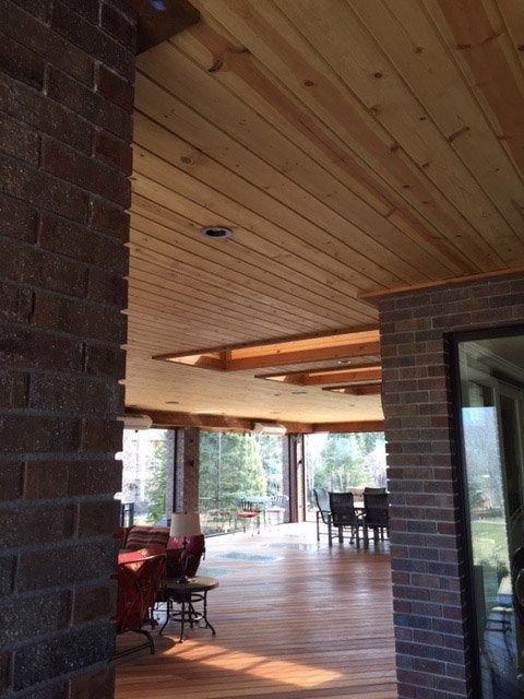 Interior view of a room with brick walls, a wood-paneled ceiling, and a wooden floor. Large windows offer an outdoor view.