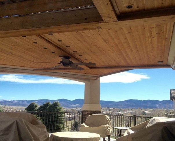 View from a covered patio overlooking a scenic vista of mountains and a blue sky. Brown wooden ceiling with a ceiling fan.