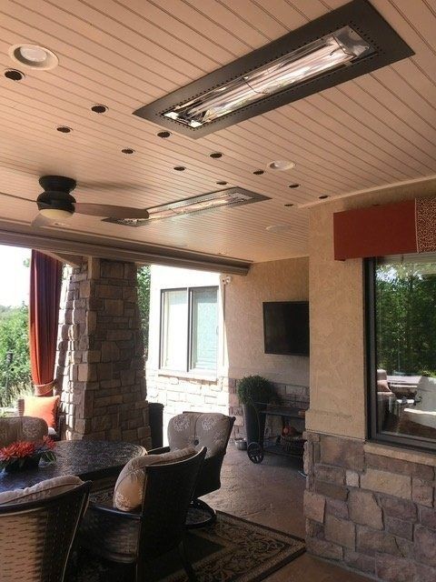 Covered outdoor patio with recessed heaters, recessed lights, ceiling fan, and stone accents.  View includes seating and a television.