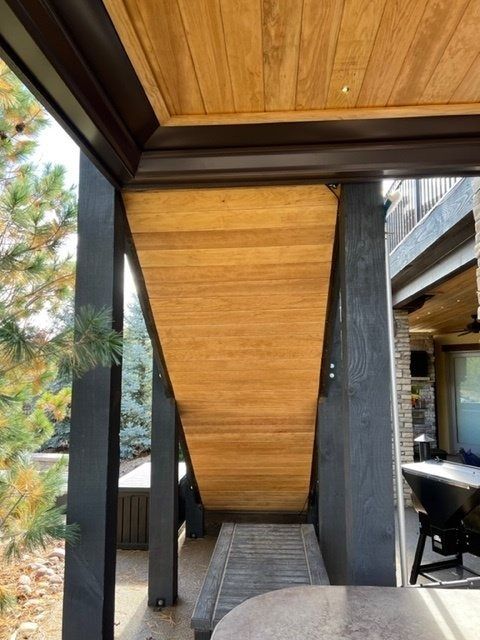 Wooden ceiling and angled support beams on a patio, surrounded by black metal columns and an outdoor view.