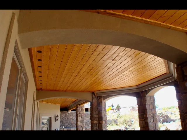 Wooden ceiling of a porch with stone columns and arched openings, bathed in natural light.
