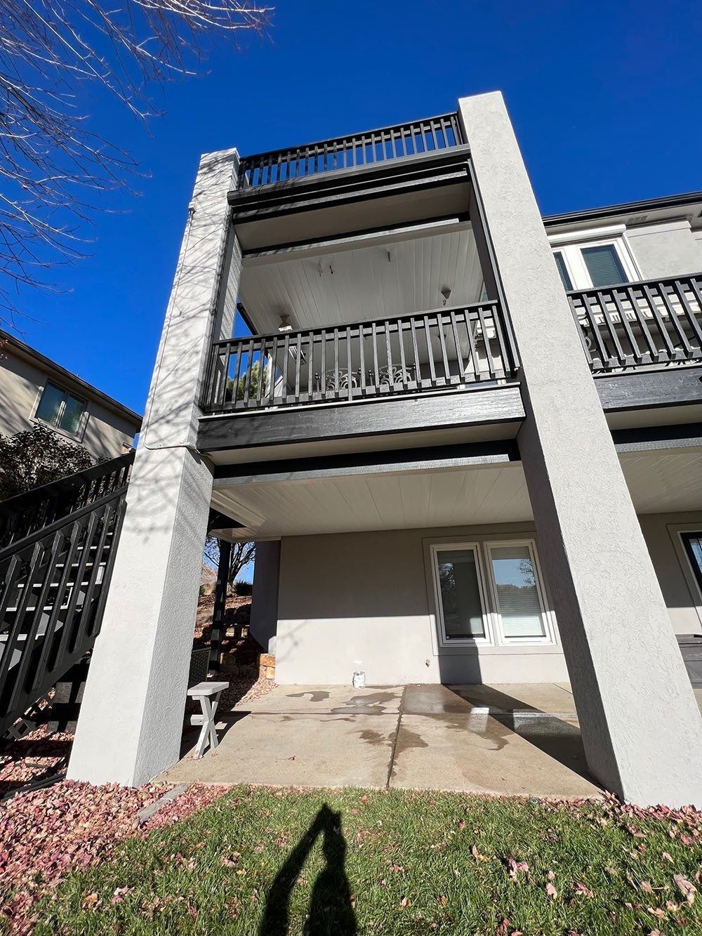 Low-angle view of a three-story building with balconies. Gray and black railings and pillars, with a bright blue sky overhead.