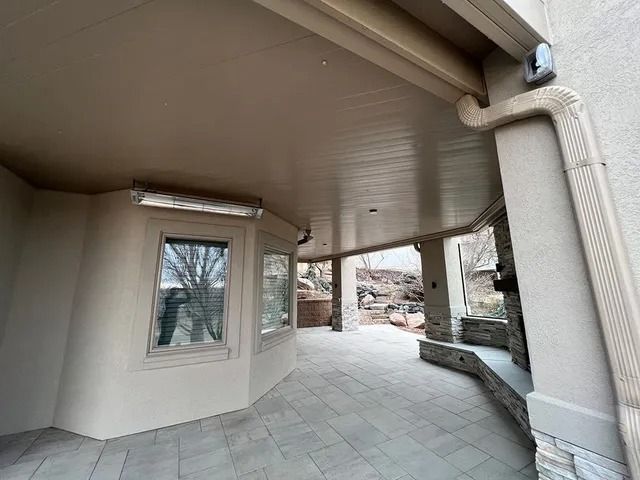 An outdoor patio with beige walls, a fireplace, and tiled floor. Windows face a view of trees and a rock formation.