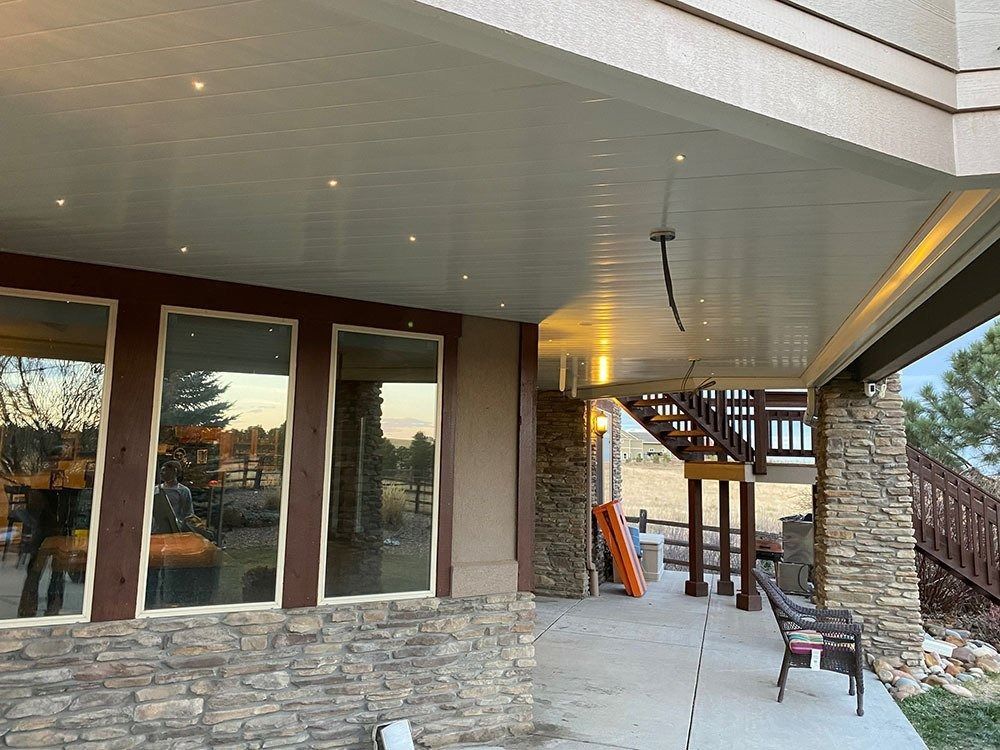 Covered patio with stone columns and recessed lighting. Large windows on the left, stairs in the background.