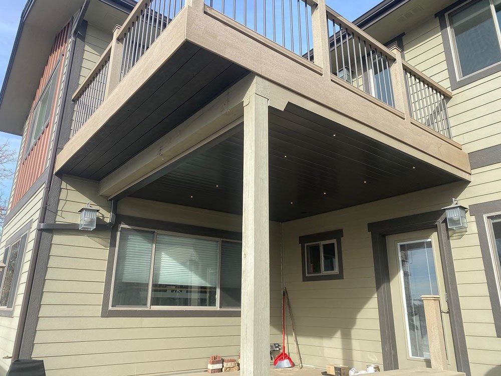 A two-story house with a deck. Beige siding, brown trim, and a brown deck with a light brown ceiling and light-colored support beams.