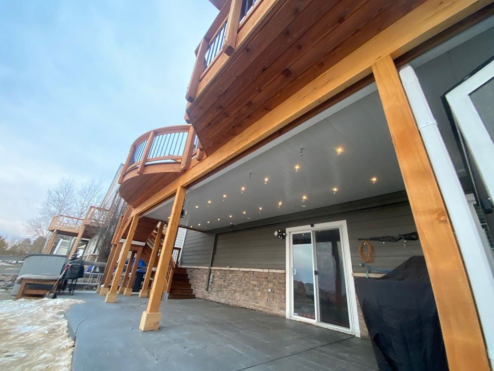 Wooden deck with a lower level, showing a sliding glass door, recessed lights, and a snowy ground.