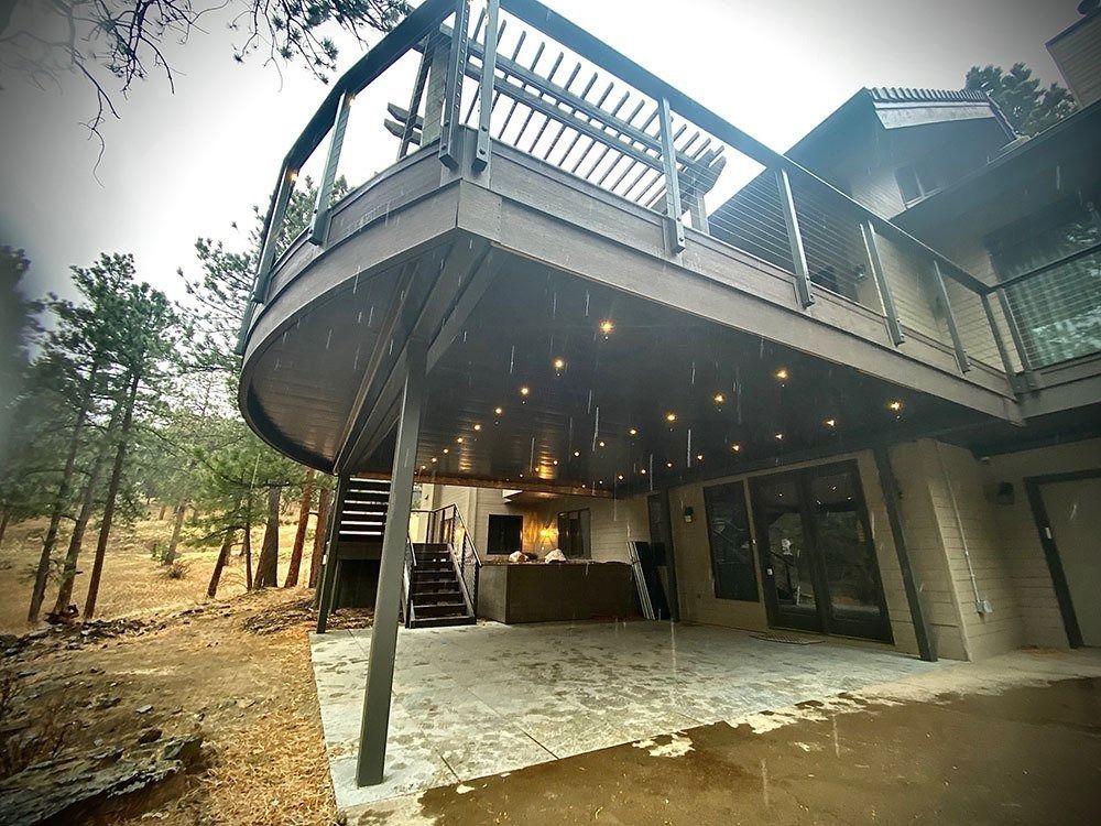 A house with a curved deck, outdoor kitchen, and stairs leading down. It's raining, and the deck has string lights.