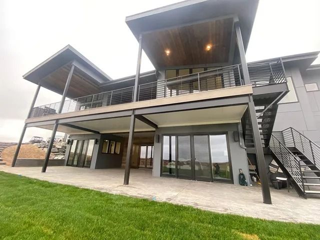 Two-story modern house with a large deck. Exterior features gray siding, black metal railings, and a staircase.