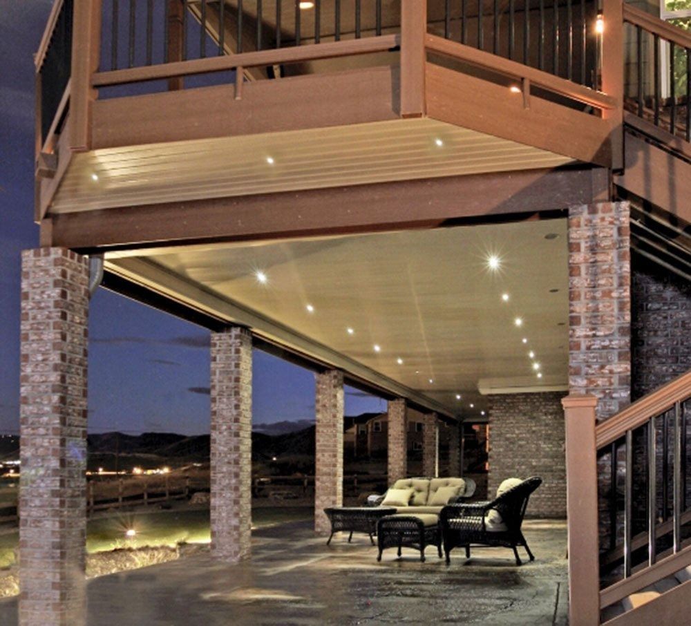 Outdoor patio with stone columns, recessed lights, and seating beneath a deck at dusk.