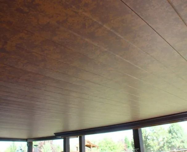 Brown wooden ceiling with horizontal grooves, viewed from below with outdoor scenery visible at the bottom.