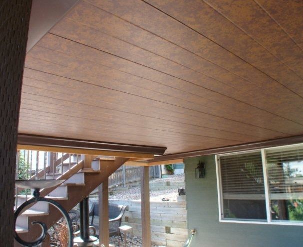 Brown-paneled ceiling of an outdoor covered deck, with a staircase and window visible.
