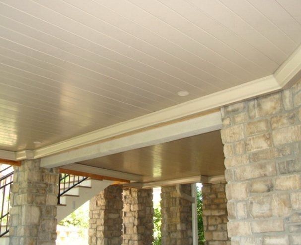 Beige-colored porch ceiling with decorative molding and stone pillars. Sunlight reflects off the glossy surface.