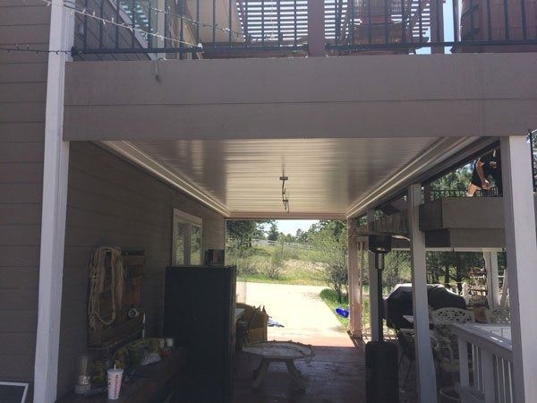 Covered patio with a light-colored ceiling and support beams; a view of a pathway and the outdoors beyond.