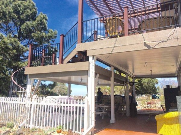 Two-story deck with a covered patio. A person stands below. The deck has a spiral staircase, black railing, and brown trim.