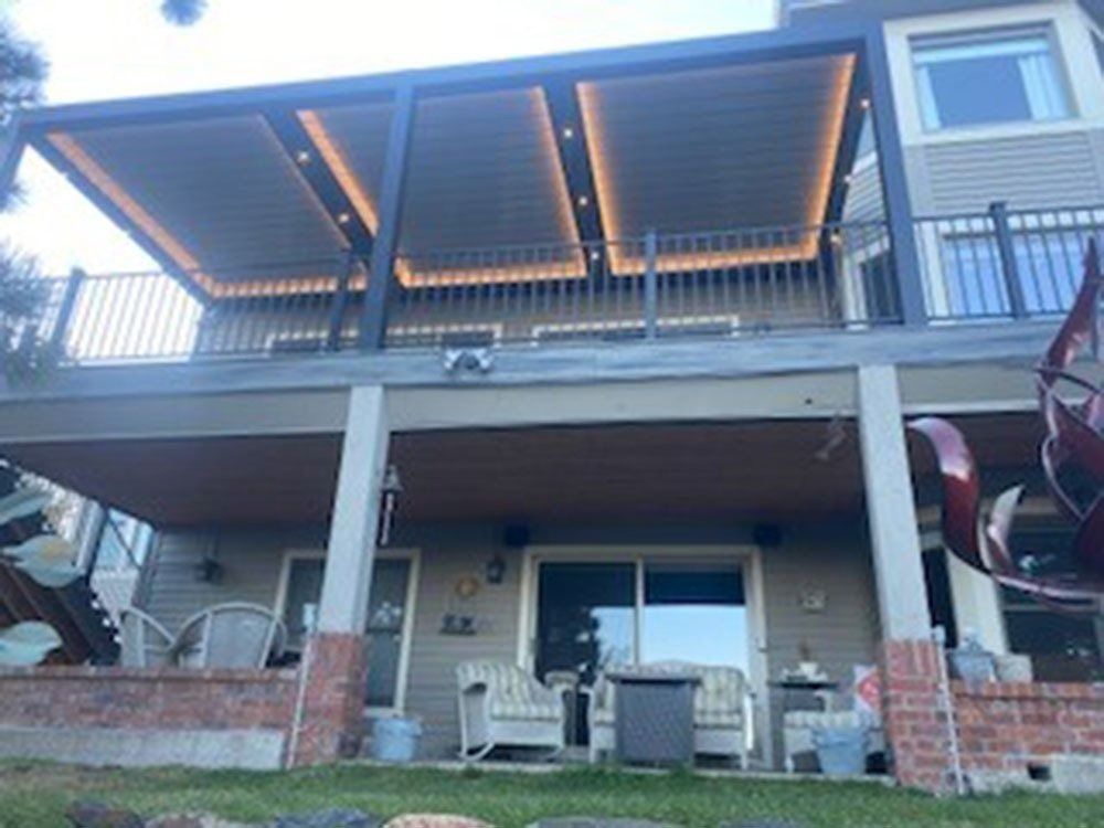 Two-story home with a deck featuring a pergola with built-in lighting. The lower level has a patio with furniture.