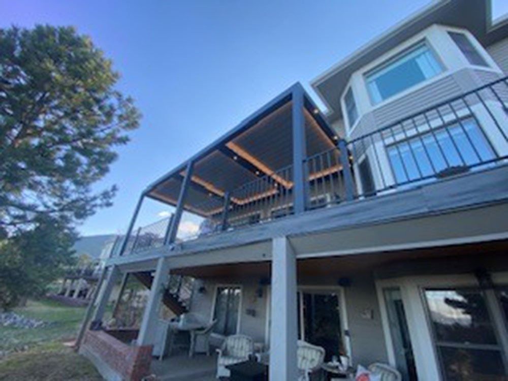 A two-story house with a deck and pergola with string lights. The sky is blue.