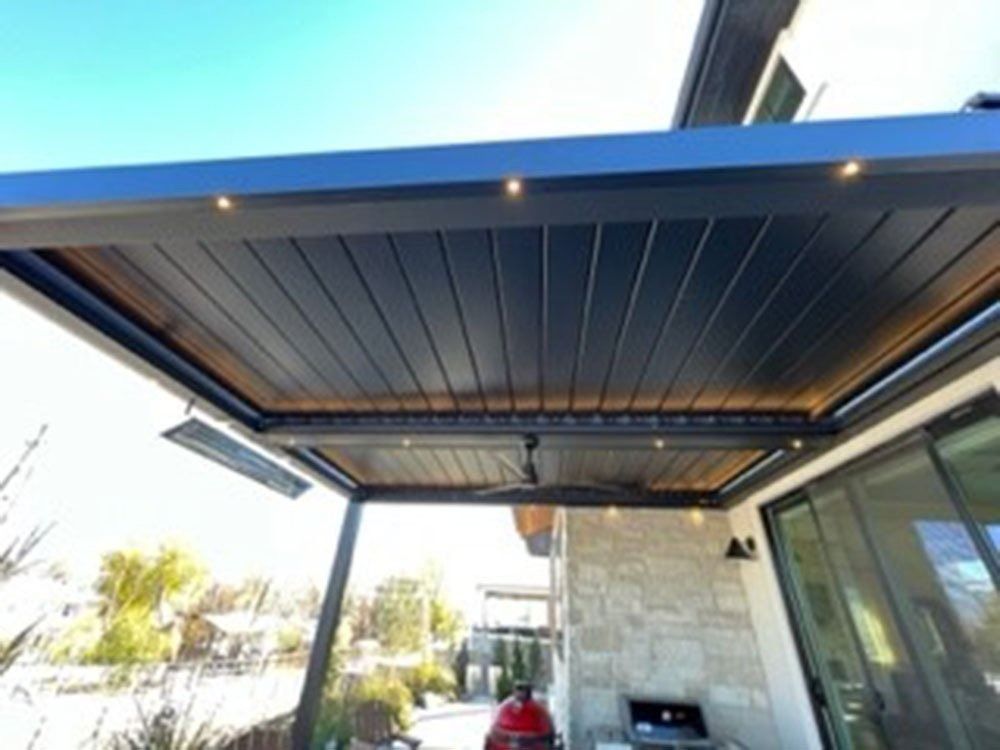 Black patio roof with built-in lights and an infrared heater, extending over an outdoor seating area with a grill.