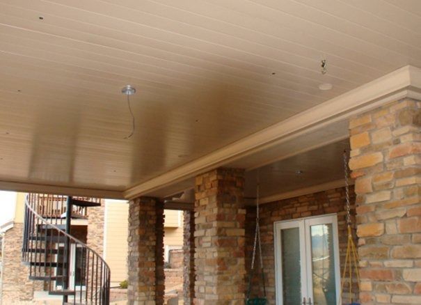 Covered outdoor patio with beige ceiling, brick columns, and spiral staircase in the background.