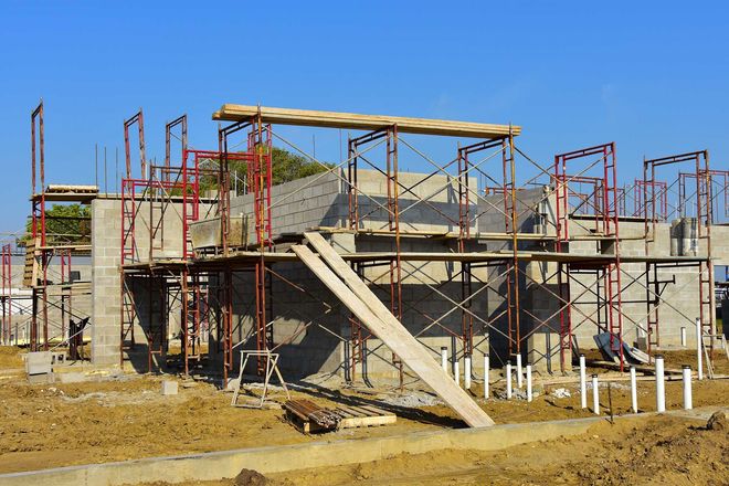 building under construction with concrete walls, scaffolding, and wooden planks