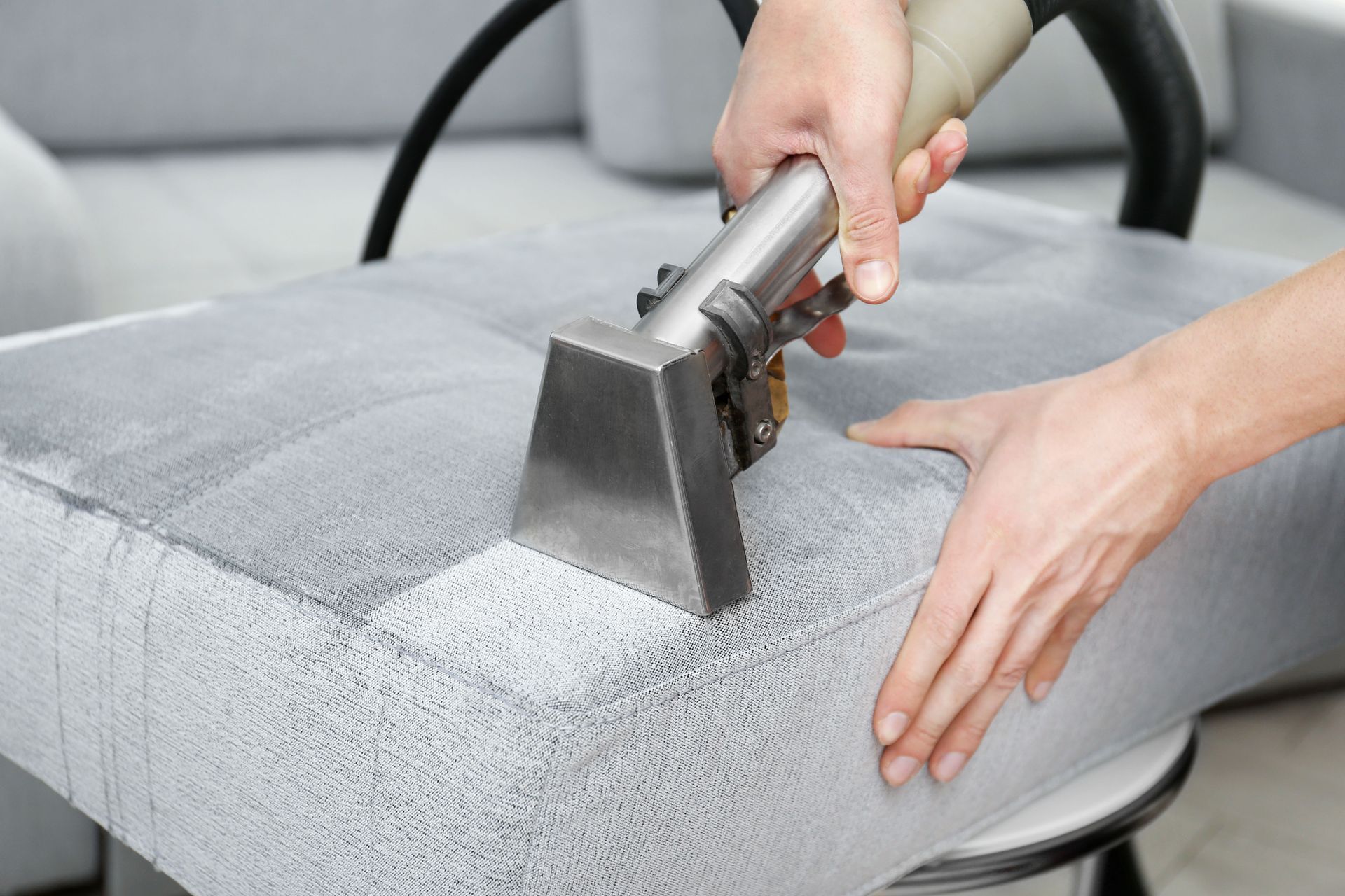 Technician using a professional upholstery cleaning tool to deep clean a light gray fabric sofa cushion.