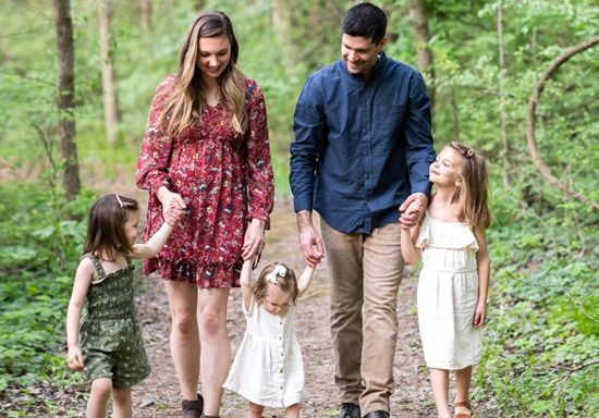 A family is walking down a path in the woods holding hands