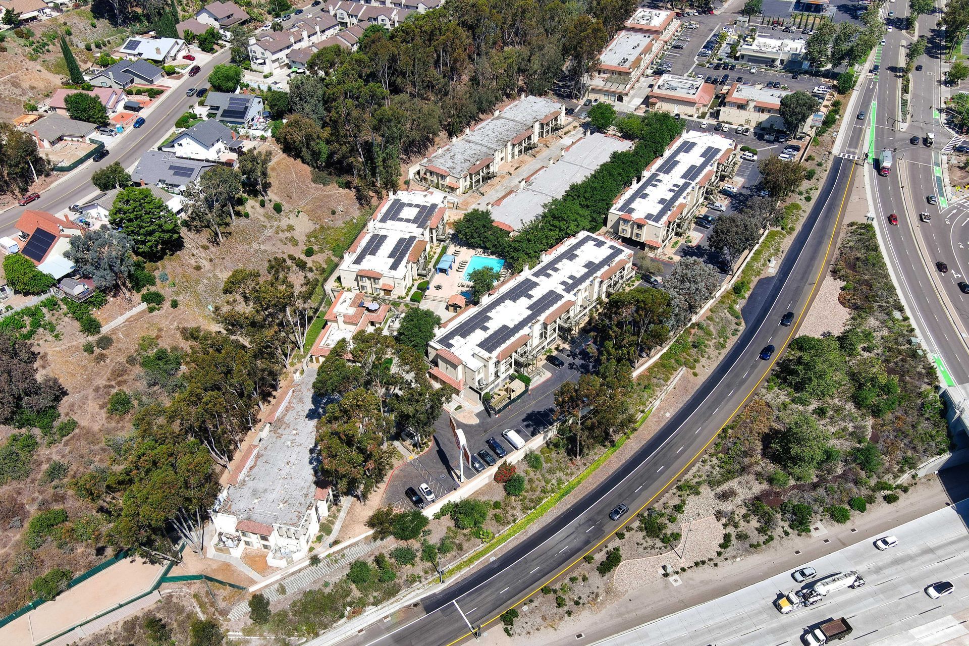 Aerial view of residential buildings with solar panels, a pool, and a highway in a suburban setting.