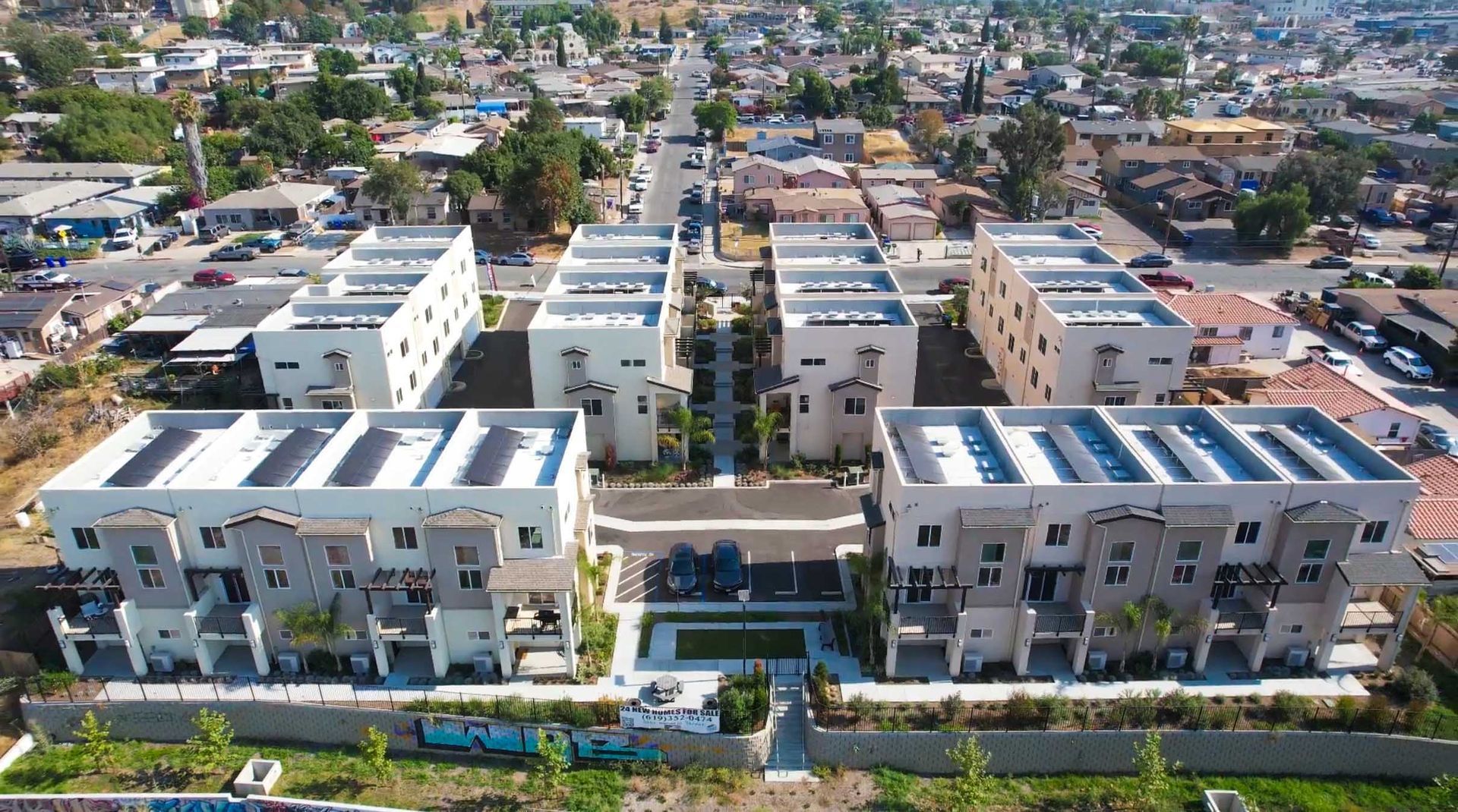 Aerial view of modern townhouses with solar panels, trees, and a street in a neighborhood.