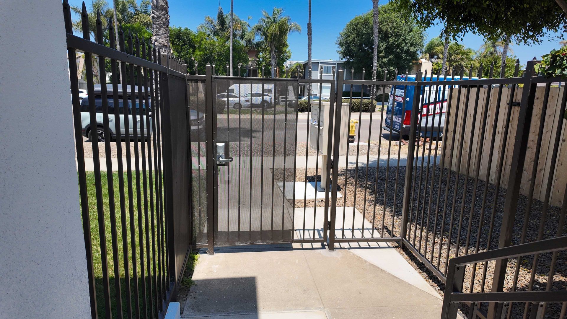 Black metal gate entrance on a sunny day; open to a parking lot.