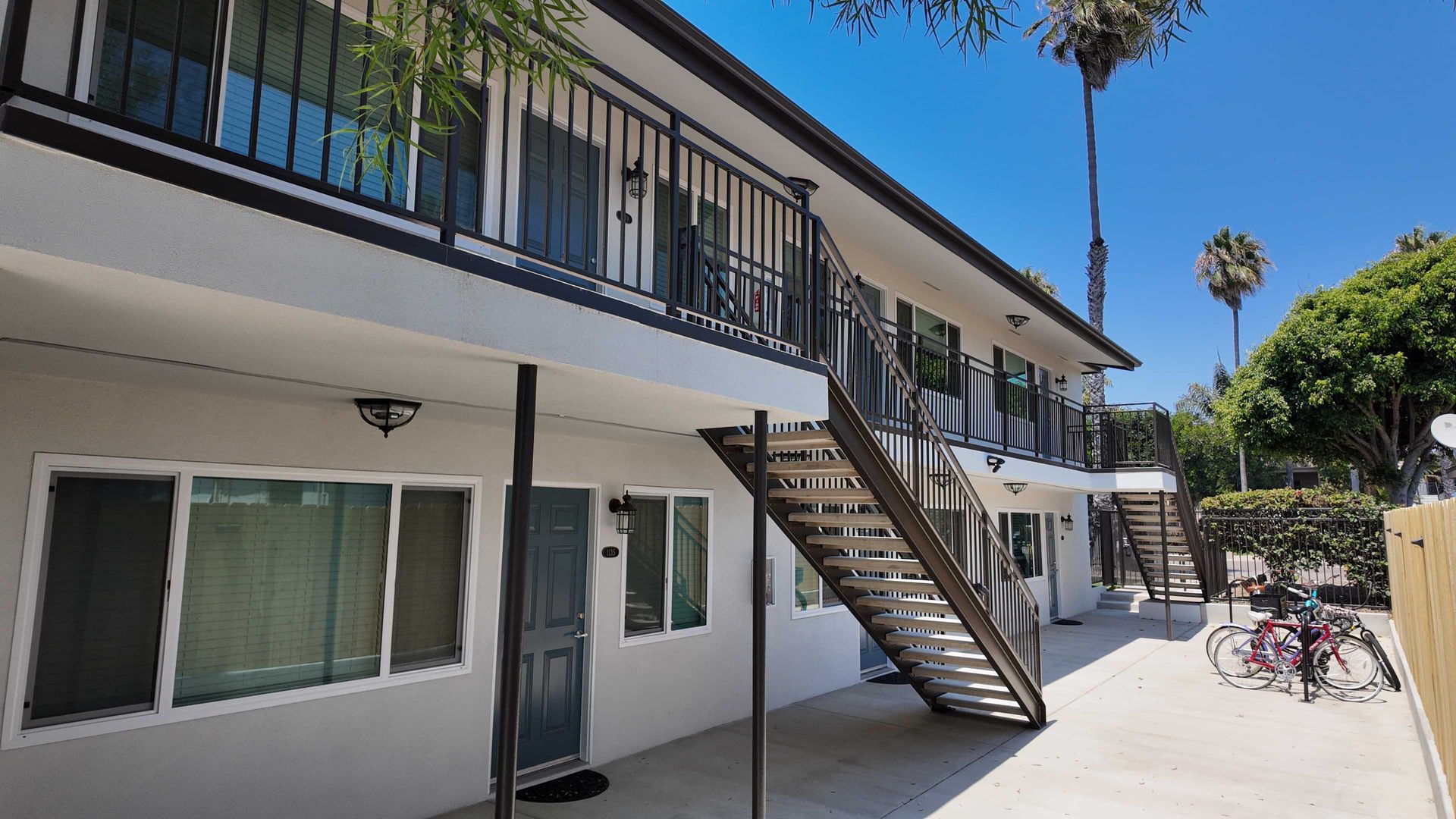 Apartment building exterior with dark metal staircases and balconies under a sunny blue sky.