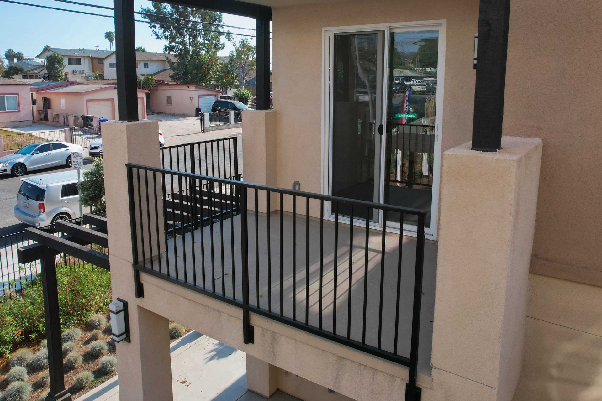 Balcony with black railing, sliding door, overlooking neighborhood with cars and houses.