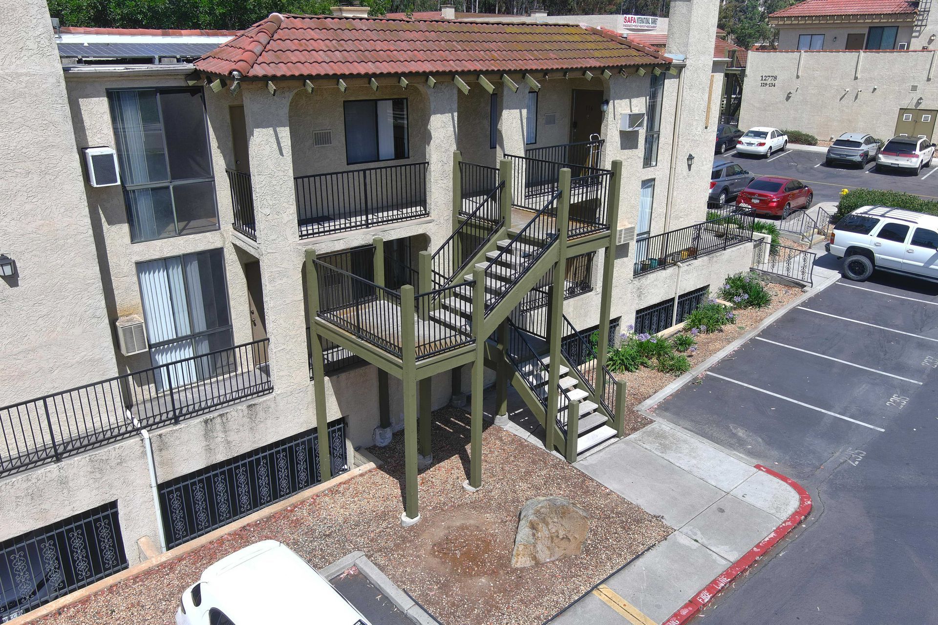 Apartment building exterior, two stories, brown tiled roof, with a staircase and parking lot.