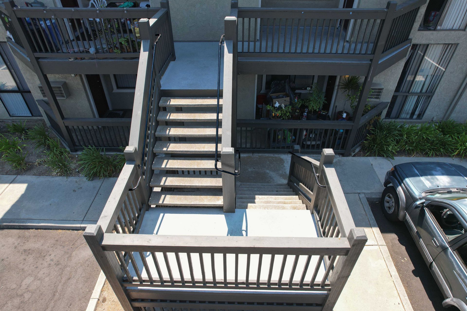 Exterior stairs leading to apartments, light gray paint, railings, a car parked nearby.
