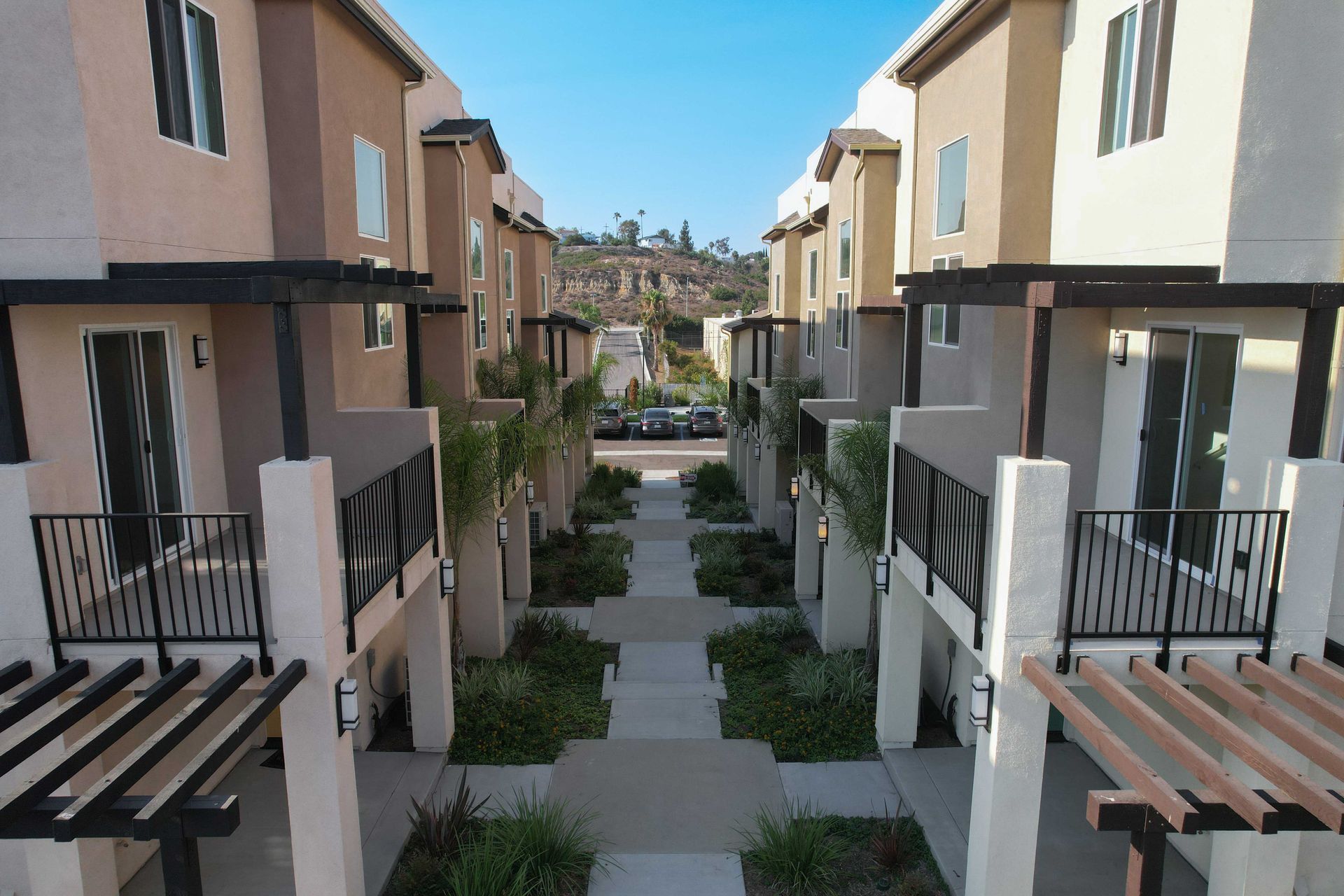 Row of townhouses with tan and brown exteriors, walkway in between, under a blue sky.