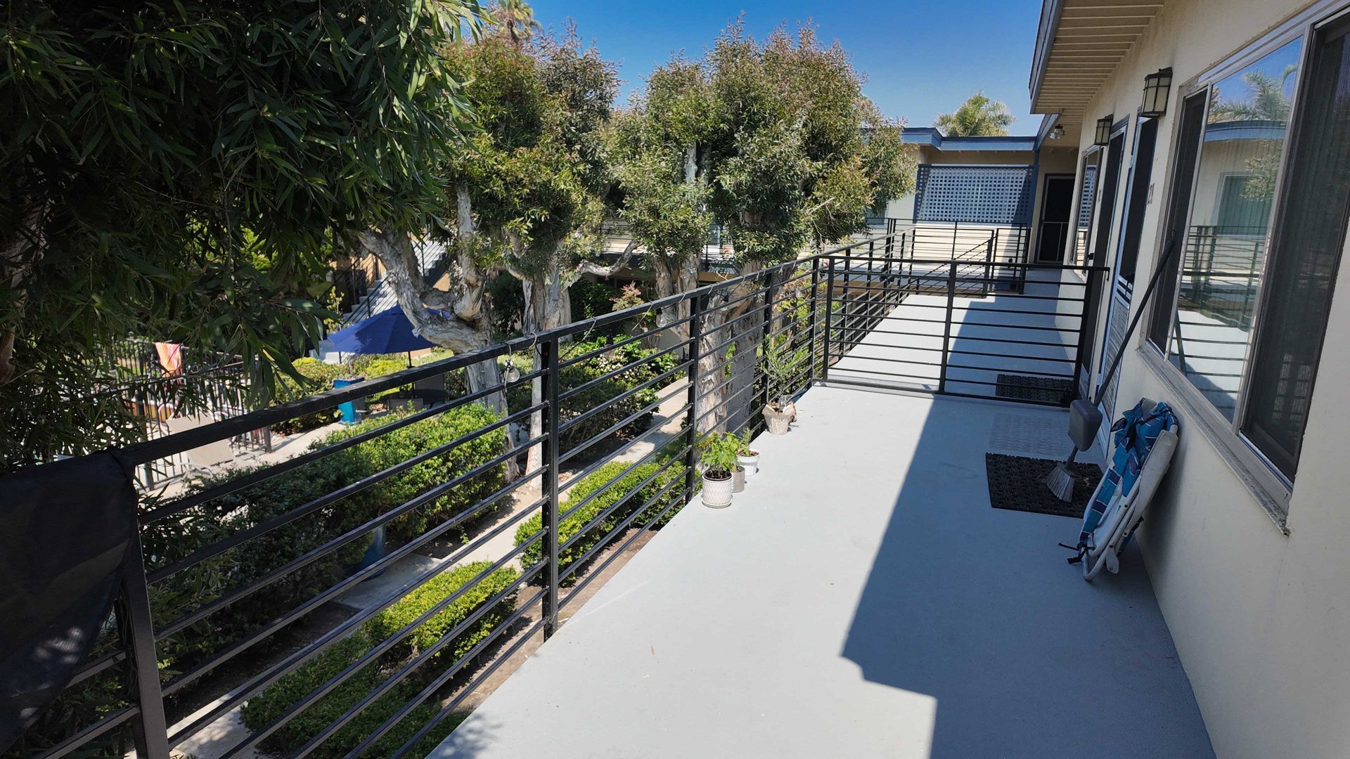 Exterior apartment walkway with black railing, gray floor, and trees.
