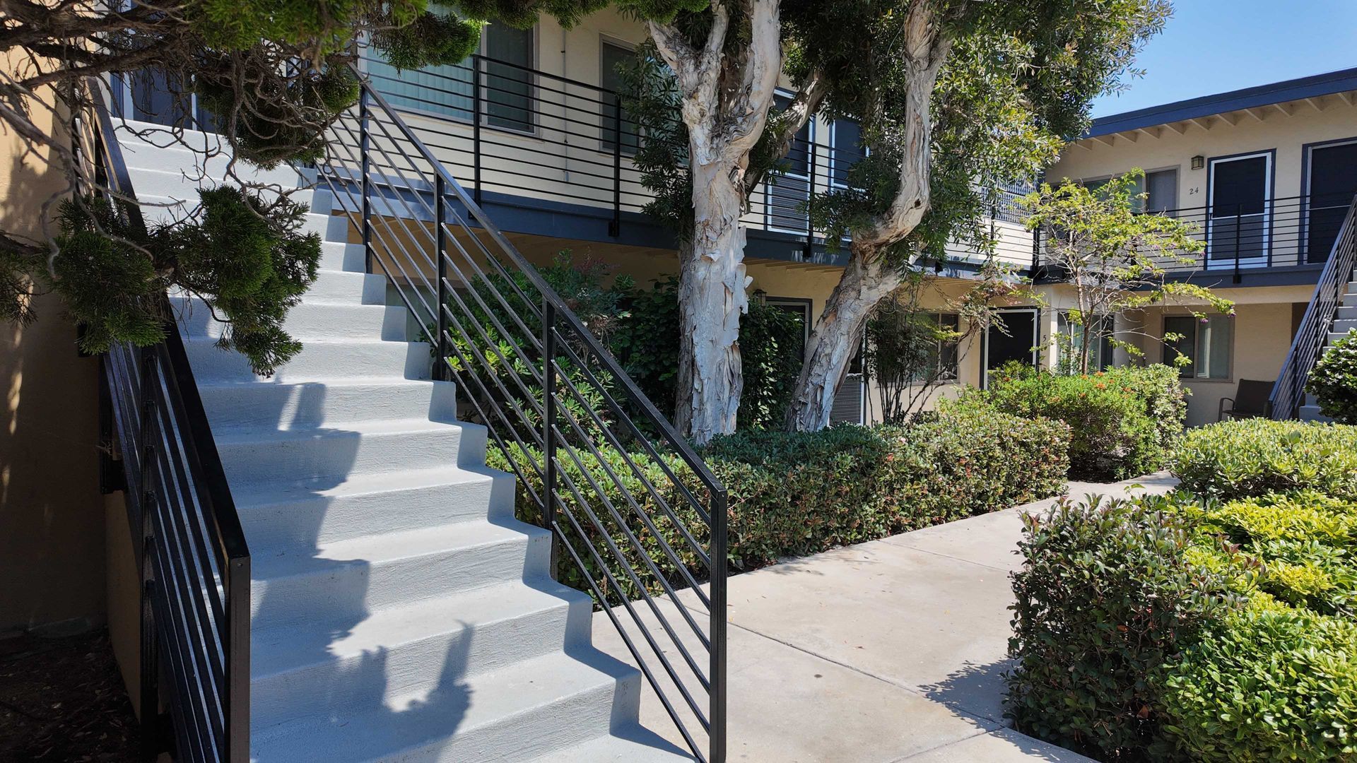Exterior of apartment building with stairs, black railing, and landscaping.