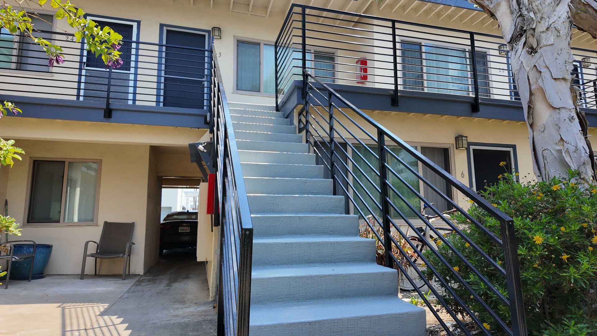 Two-story building with exterior stairs and metal railings. Gray steps lead up to a second-floor landing.