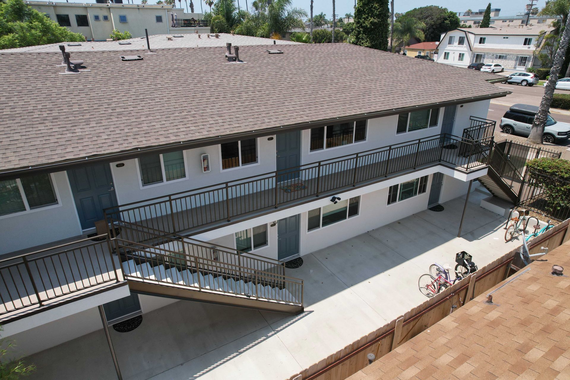 Apartment building with brown tile roof and blue doors, with outdoor staircases and walkway.