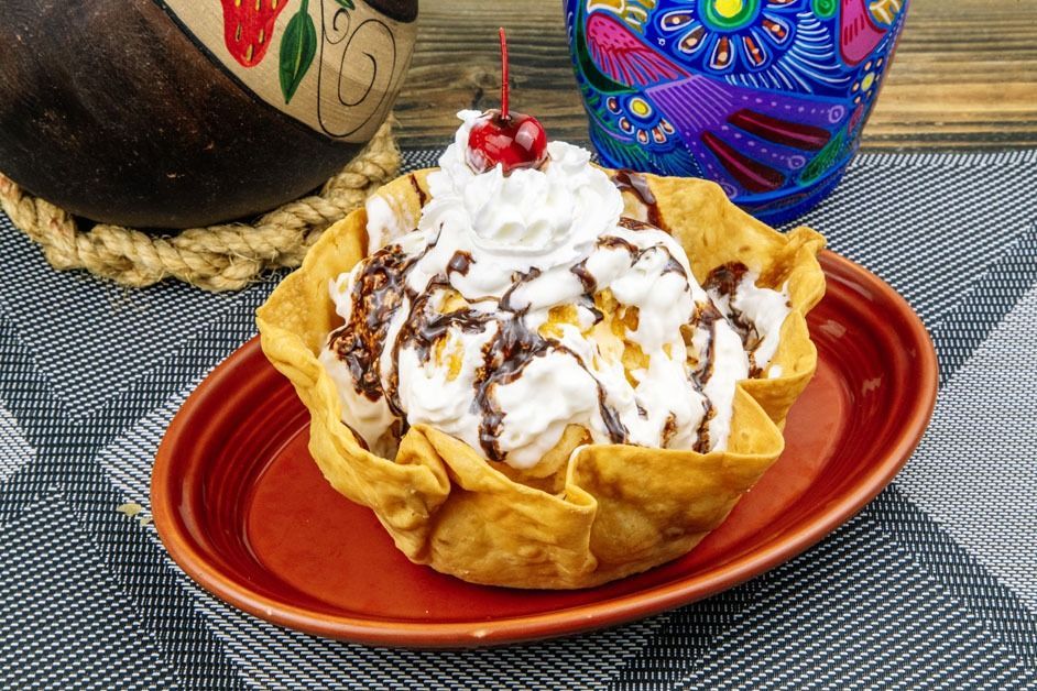 A tortilla bowl filled with ice cream and whipped cream with a cherry on top.