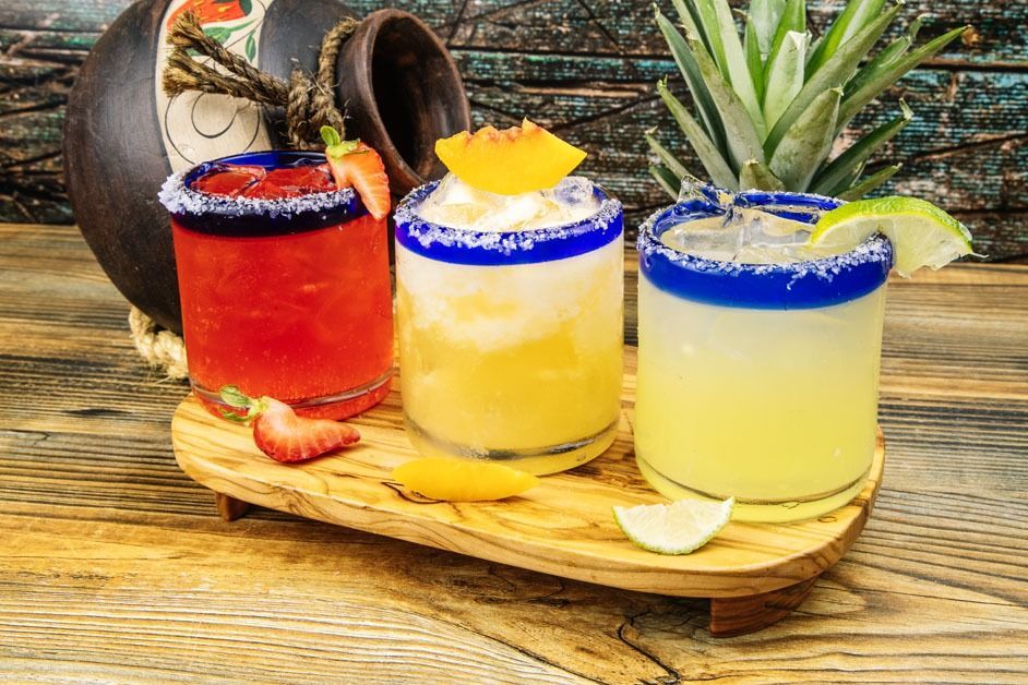 Three margaritas are sitting on a wooden tray on a wooden table.