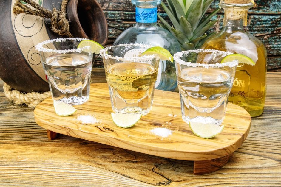 Three shot glasses of tequila on a wooden tray on a wooden table.