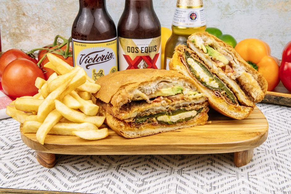 A sandwich and french fries are on a wooden cutting board.